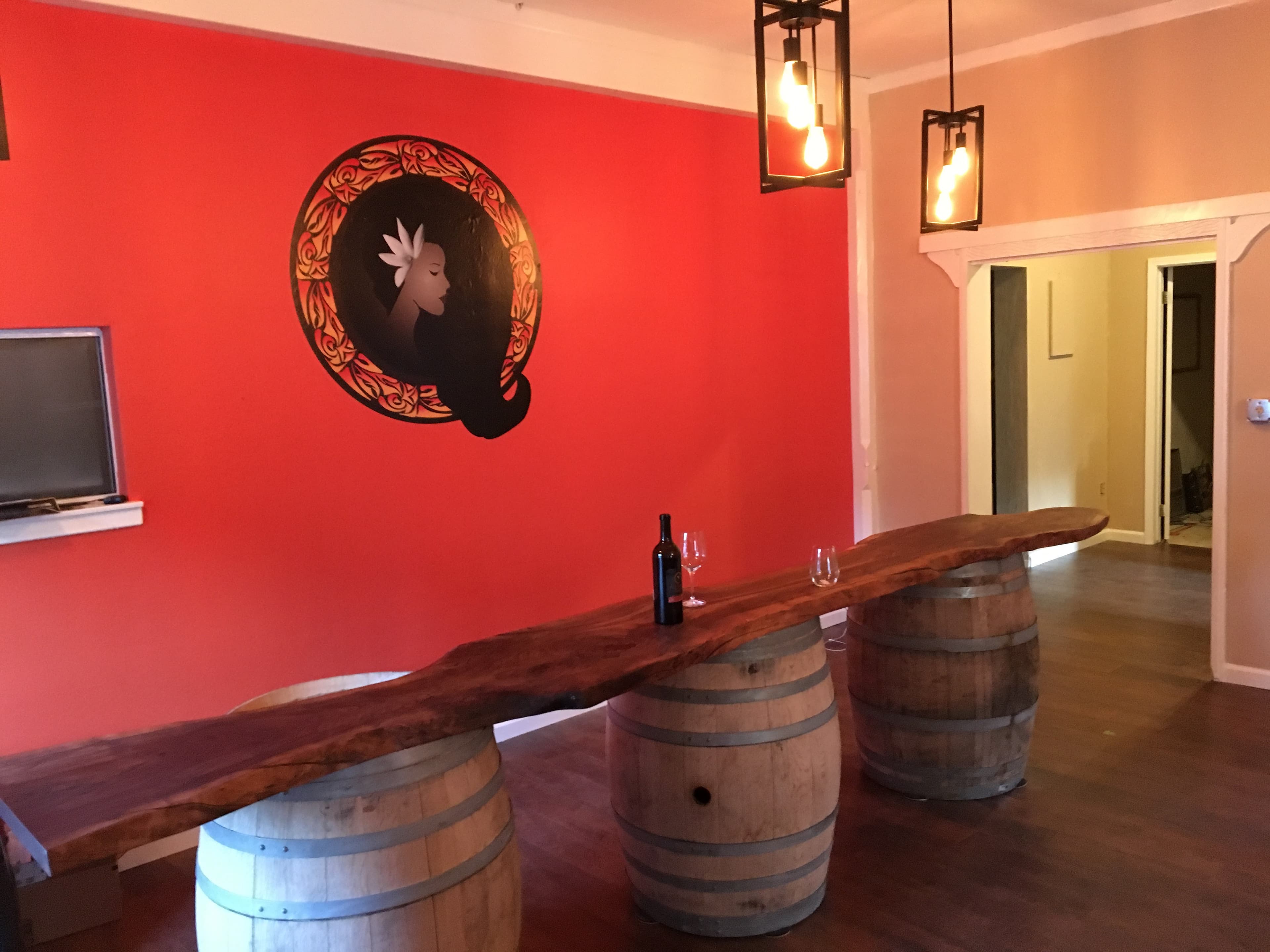 The Polynesian Girl tasting room — live-edge bar on wine barrels with the painted logo wall